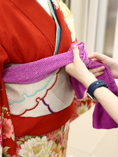 写真：着付けをされる赤い振袖を着た女性