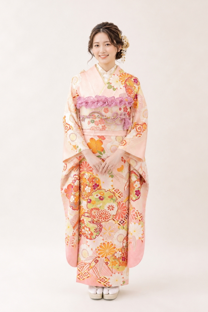 淡いピーチピンクに、橙色の菊や多彩な古典柄が映える振袖姿。